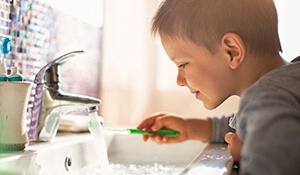 Young boy running water over toothbrush