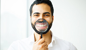 man in white shirt holding magnifying glass to smile