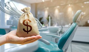 A hand holding a money bag in front of teal dental chair