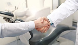 Dentist and patient shaking hands in front of dental chair