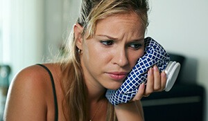 Young woman holds ice bag to face