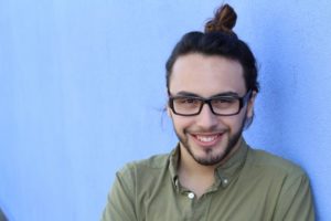 young man with small teeth smiling in front of a blue background 