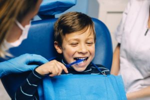 little boy brushing teeth in dental chair 